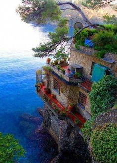 an old house on the edge of a cliff by the ocean with plants growing out of it