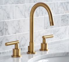 a bathroom sink with two brass faucets and marble wall tiles in the background