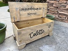 a wooden box with writing on it sitting next to two green planters and a brick wall