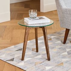 a glass table with a book on it in front of a gray chair and white rug