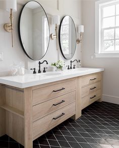 a bathroom with two sinks and three mirrors on the wall above them, along with black tile flooring