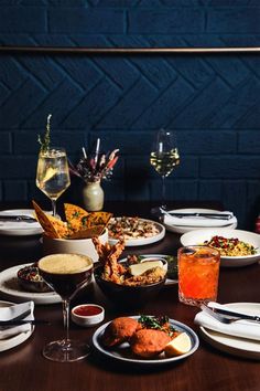 a wooden table topped with plates and bowls filled with different types of food next to wine glasses