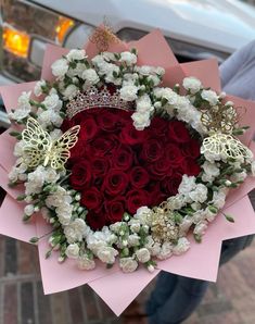 a heart - shaped bouquet with roses and butterflies is held in front of a parked car