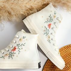 two pairs of white shoes with flowers on them next to a straw hat and fur