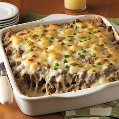 a casserole dish with meat, cheese and green onions in it on a wooden table