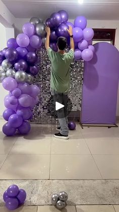 a man standing in front of a bunch of purple and silver balloons on the floor