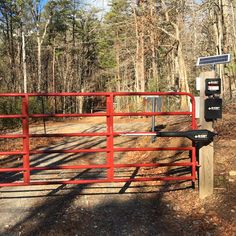 a red gate with a solar panel on it in the middle of a wooded area