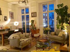 a living room filled with lots of furniture next to tall windows and plants on the wall