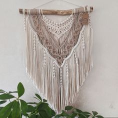 a macrame hanging on a wall next to a potted plant and wooden stick