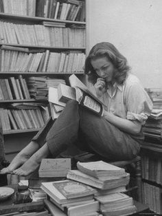 a woman sitting on the floor reading a book in front of a pile of books