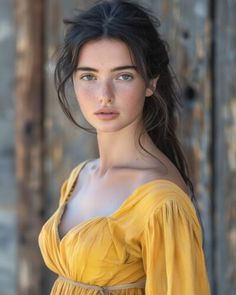 a young woman in a yellow dress poses for a photo by a wooden wall with her hair pulled back