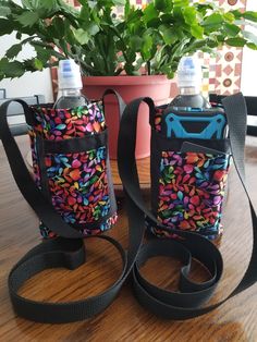 two water bottles sitting on top of a wooden table next to a potted plant