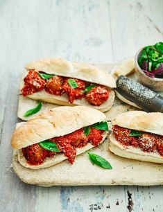 several sandwiches with meat and sauce on a cutting board