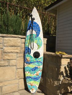 a surfboard is propped up against a stone wall and has a mosaic design on it