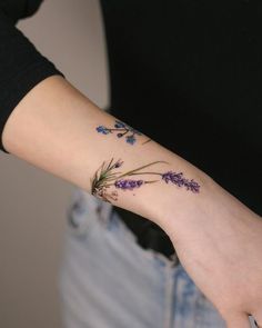 a woman's arm with purple flowers on the left side of her wrist and small bluebells on the right hand