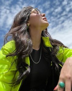 a woman with long hair and glasses is looking up into the sky while wearing a yellow jacket