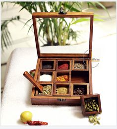 an open wooden box filled with spices on top of a white table next to a potted plant