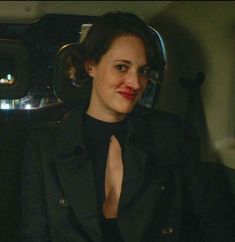 a woman with red lipstick sitting in the back seat of a car wearing a black suit