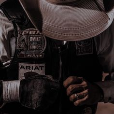 a man wearing a hat and vest with patches on it's chest is holding his hands together