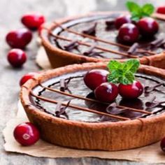 two chocolate tarts with cherries on top and garnished with green leaves