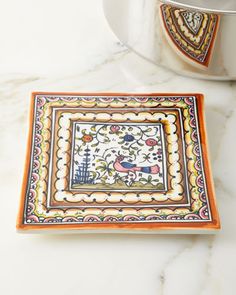 an orange and white square plate on a marble counter top next to a potted plant