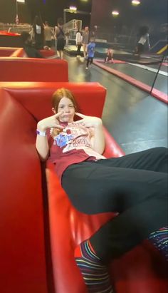 a woman sitting on top of a red couch in a bowling alley with her legs crossed