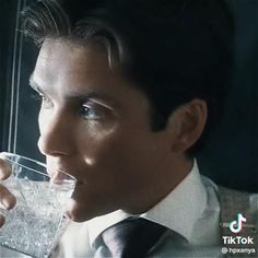 a man drinking water from a glass in front of his face and looking off to the side