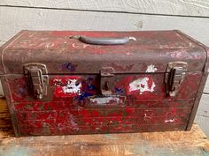 an old, rusted metal box sitting on top of a wooden table next to a wall