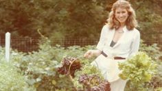 a woman standing in the middle of a garden with lettuce and carrots