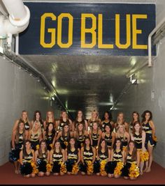 a group of cheerleaders posing for a photo in front of the go blue sign