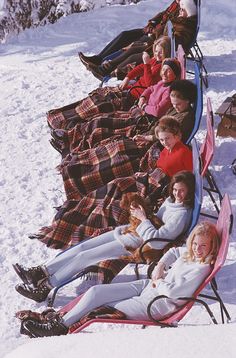 people sitting on lawn chairs in the snow with blankets over their heads and feet,