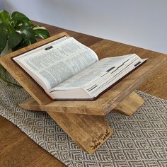 an open book sitting on top of a wooden stand next to a potted plant