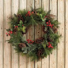 a wreath with pine cones and red berries hanging on a wooden wall next to a door