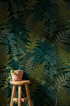 a plant sitting on top of a wooden stool in front of a green wallpaper