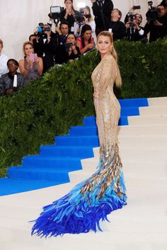 the model is dressed in a gold and blue gown with feathers on her tail, as she