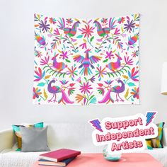 a colorful tapestry hanging on the wall above a white couch with pillows and a pink table