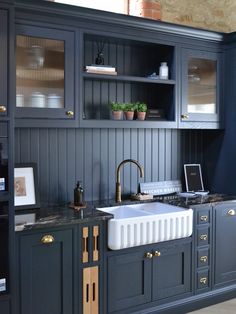 a kitchen with dark blue cabinets and gold pulls on the sink, along with an open shelving unit