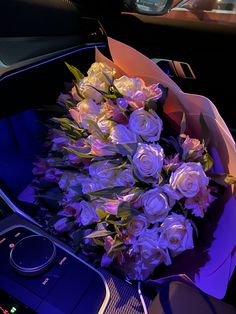 a bouquet of white roses sitting in the center console of a car with blue lighting