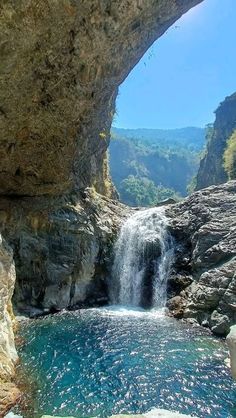 there is a waterfall coming out of the side of a rock formation with blue water