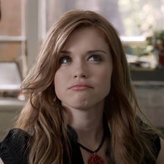 a woman with long brown hair wearing a black shirt and necklace looking at the camera