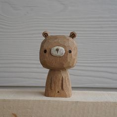 a small wooden bear sitting on top of a piece of wood next to a white wall