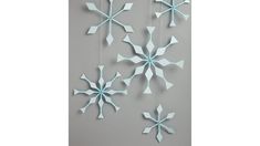 three snowflakes hanging from strings on a gray wall, one is blue and the other is white