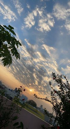 the sun is setting behind some clouds in the sky over a cityscape and trees