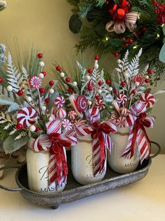 three mason jars filled with candy canes and greenery are sitting on a tray