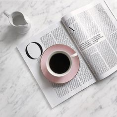 a cup of coffee sitting on top of a table next to an open book and a mug