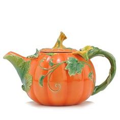 an orange pumpkin shaped tea pot with green leaves on the rim and handle, sitting on a white surface