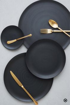 three black plates with gold forks and spoons