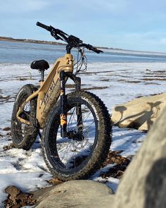 a bike parked on top of snow covered ground next to rocks and water in the background