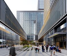 many people are walking around in an open area with tall buildings on either side of the walkway