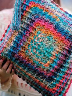 a woman holding up a colorful crocheted pillow